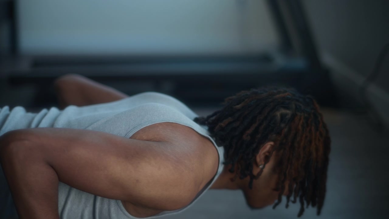 A young man with dreadlocks doing push ups at home