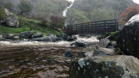 cascada río rocoso agua que fluye a cámara lenta en cascada bajo el puente de madera en el parque nacional