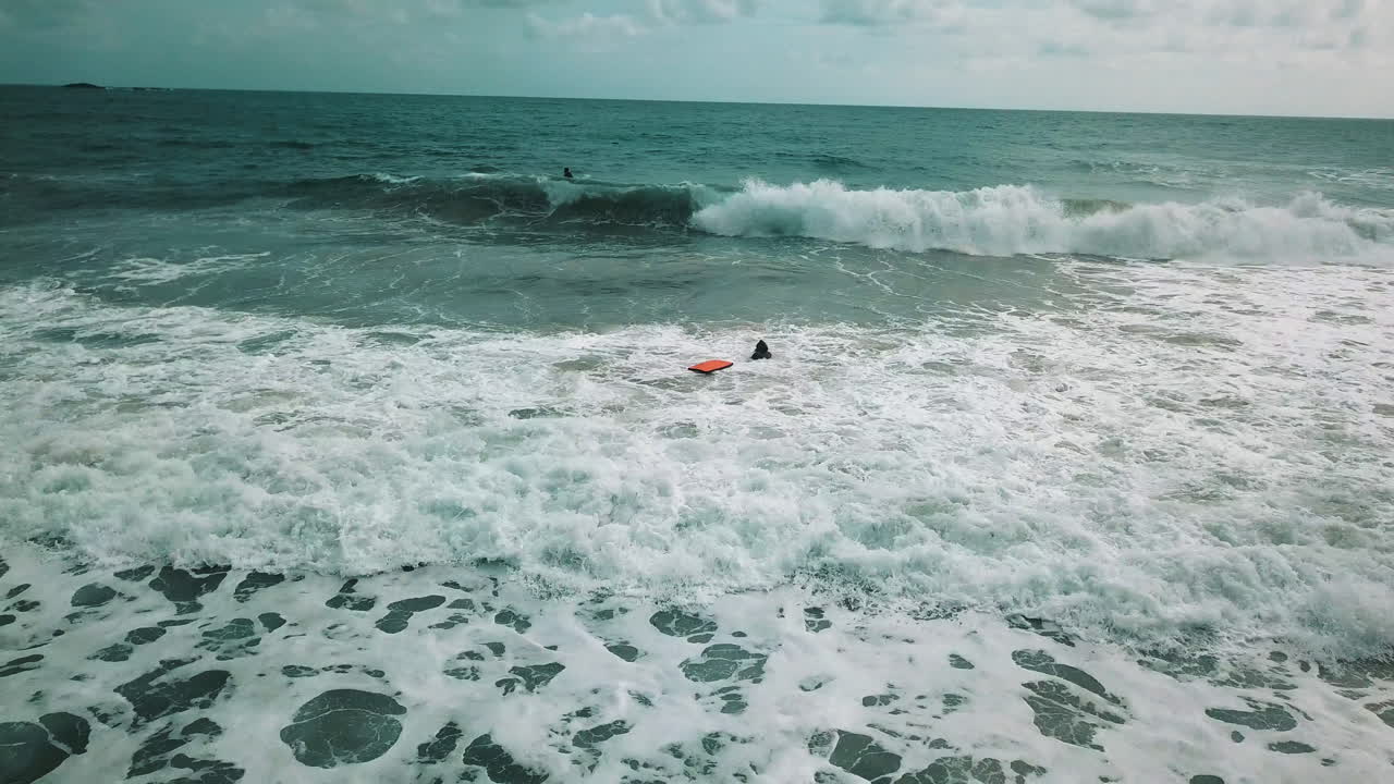 A group of people surfing, one of them takes a wave and plunges into the water when the wave breaks in the middle of a lot of foam
