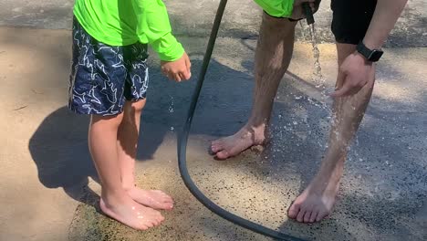 dad washing son off with water after playing at the sandy beach.