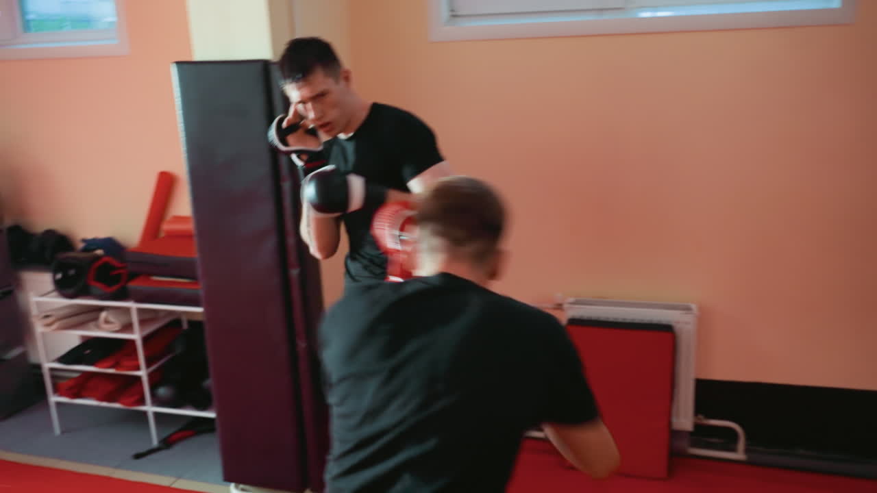 Pugilist wearing red gloves faces opponent inside gym, holding strong guard stance with focus, determination, and readiness, displaying combat discipline, athletic energy, and concentration