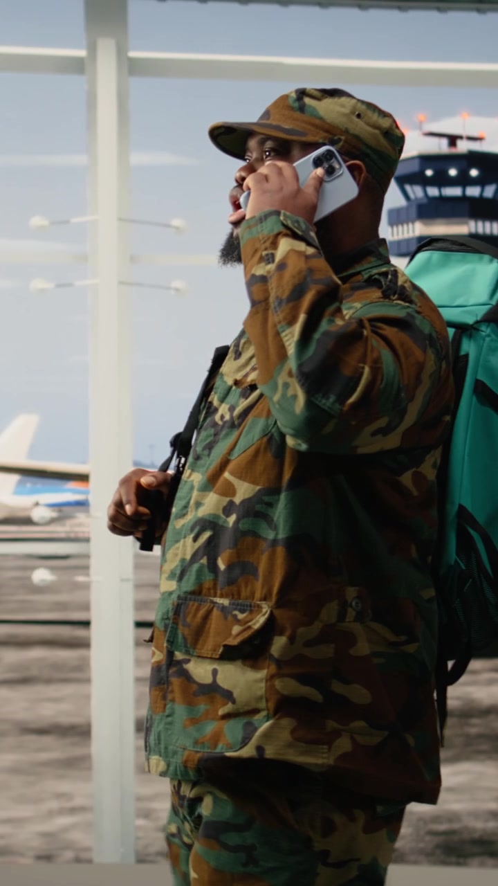 Video verticale. Soldato dell'esercito in aeroporto che conversa al telefono con lo smartphone.