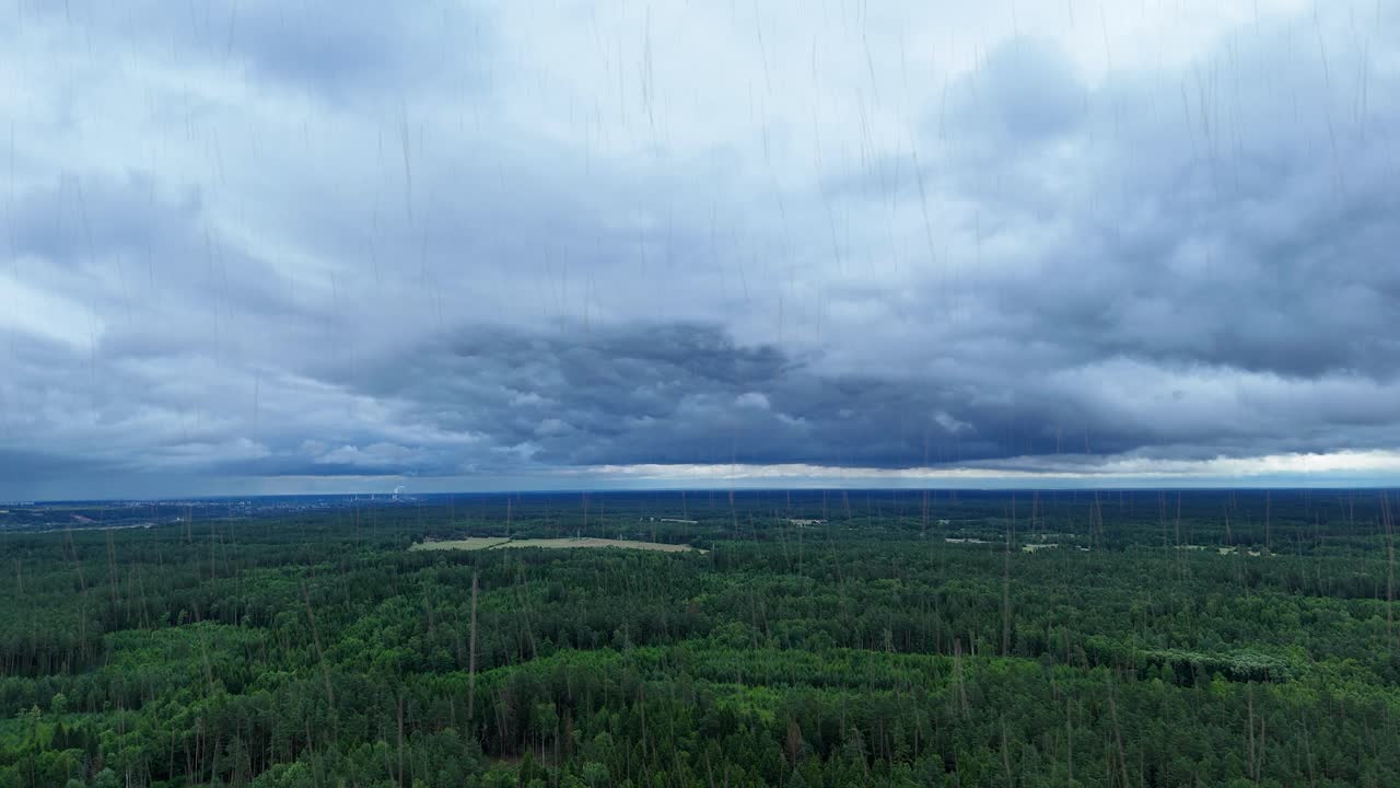 Dark storm clouds and pouring rain over green forest of Lithuania, aerial view