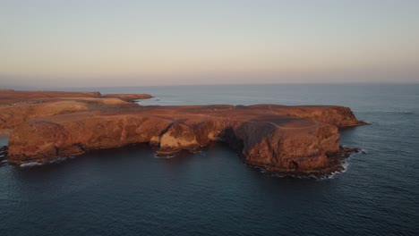 Die-Felsigen-Klippen-Der-Insel-Papagayo-Sehen-Bei-Sonnenuntergang-Rot-Aus,-Während-Die-Wellen-Sanft-Gegen-Sie-Schlagen