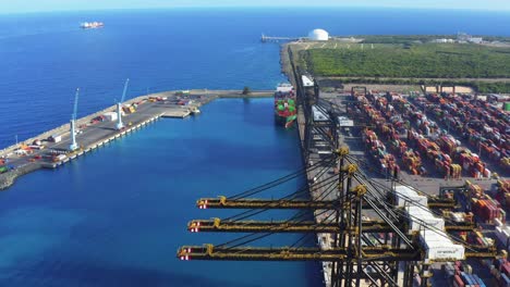 colorful cargo containers stacked at shipyard terminal by tall cranes with view of vast blue ocean sea water, punta caucedo, dominican republic, aerial