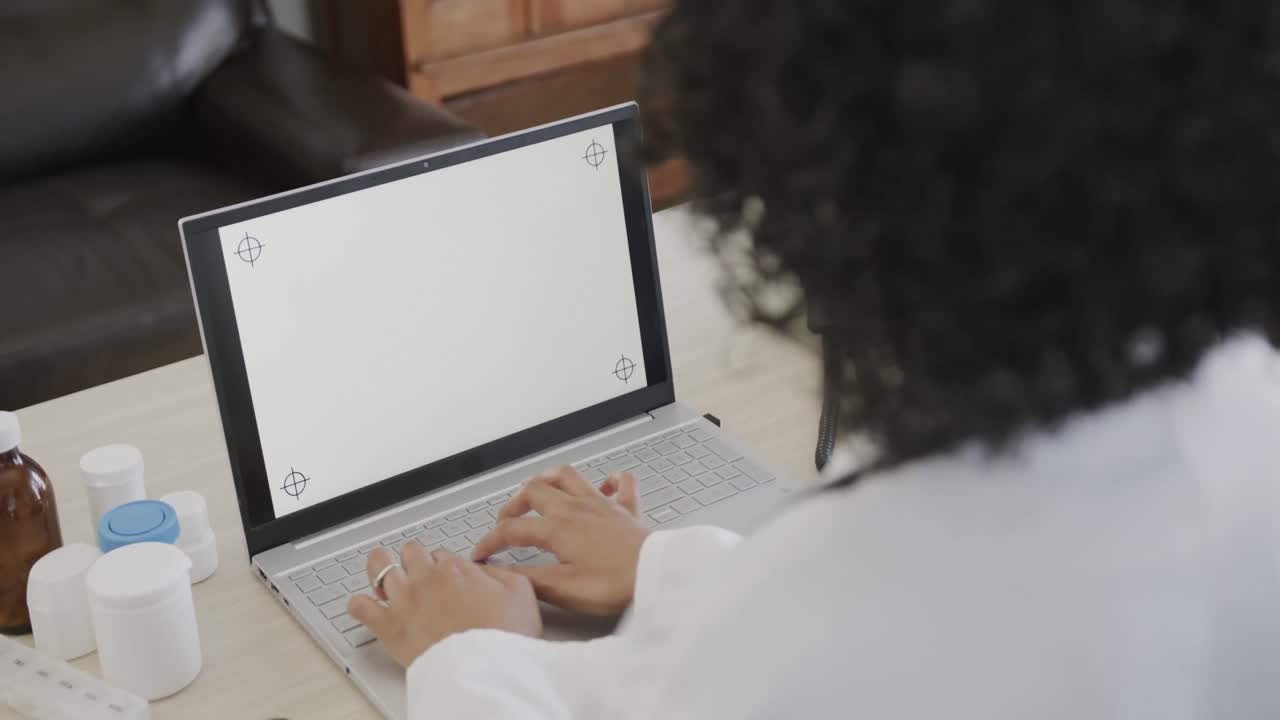 doctora biracial sentada en un escritorio y usando una computadora portátil con espacio para copiar, cámara lenta