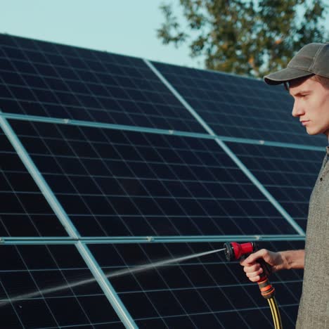 young man washes solar panels with a hose