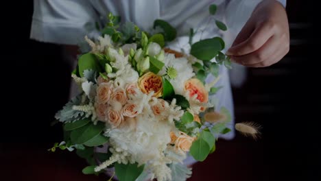 Bride-holding-and-arranging-a-bouquet-of-white-and-peach-flowers-with-green-foliage