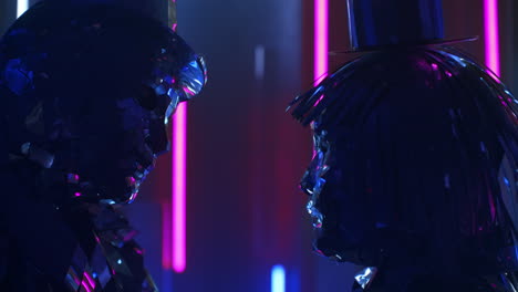 close up.two dancers a man and a woman standing opposite each other shaking in time to the music synchronously head in sparkling mirrored costumes in blue violet color of shimmering neon.