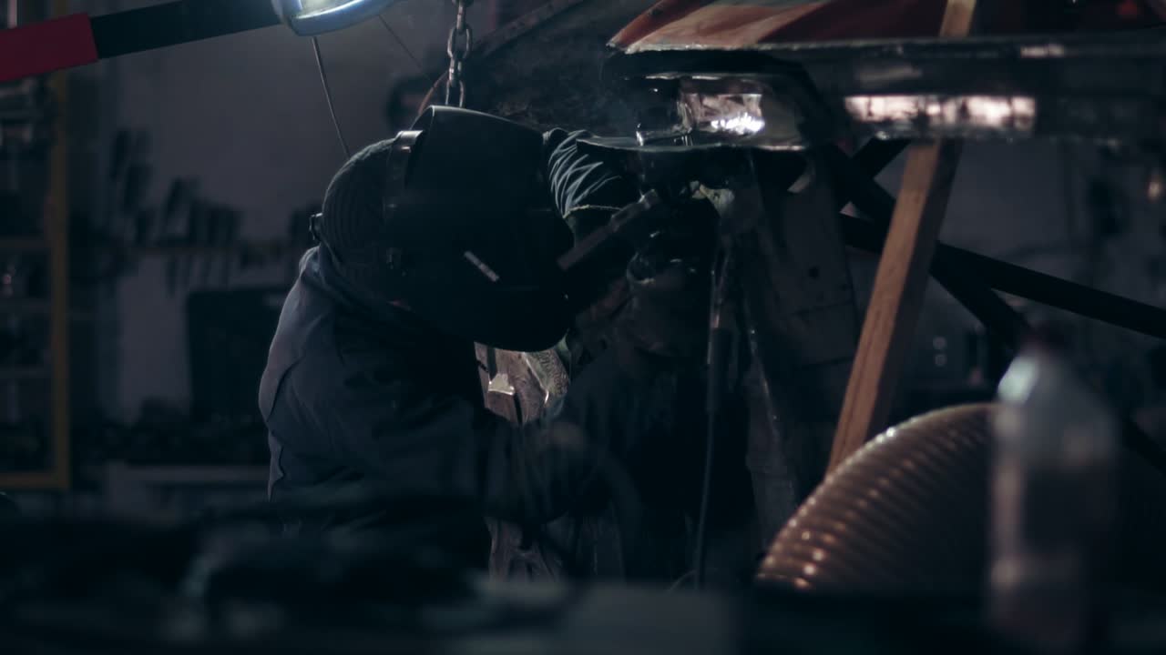 Welder working on bottom side of the car at a mechanical hangar.