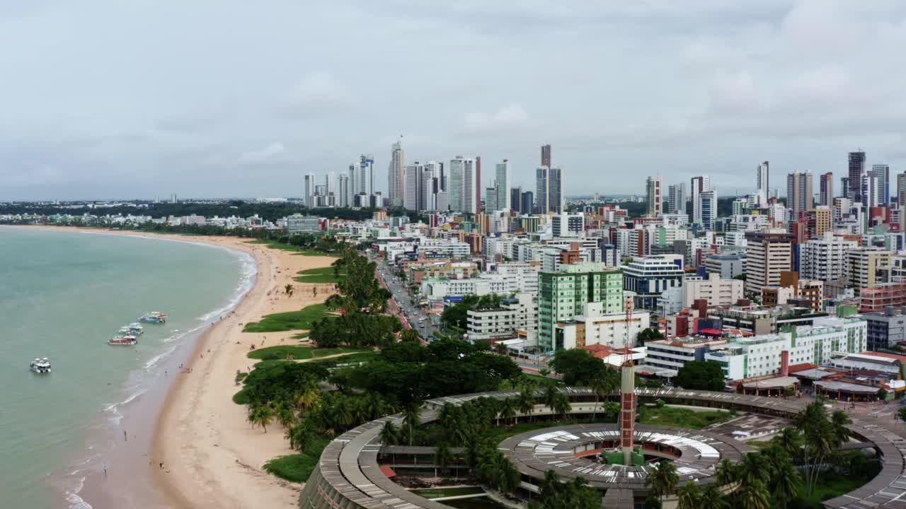 Dolly in aerial drone shot of a large round building on the beach in the colorful tropical beach capital city of Joao Pessoa in Paraiba, Brazil from the Tambaú neighborhood on an overcast morning