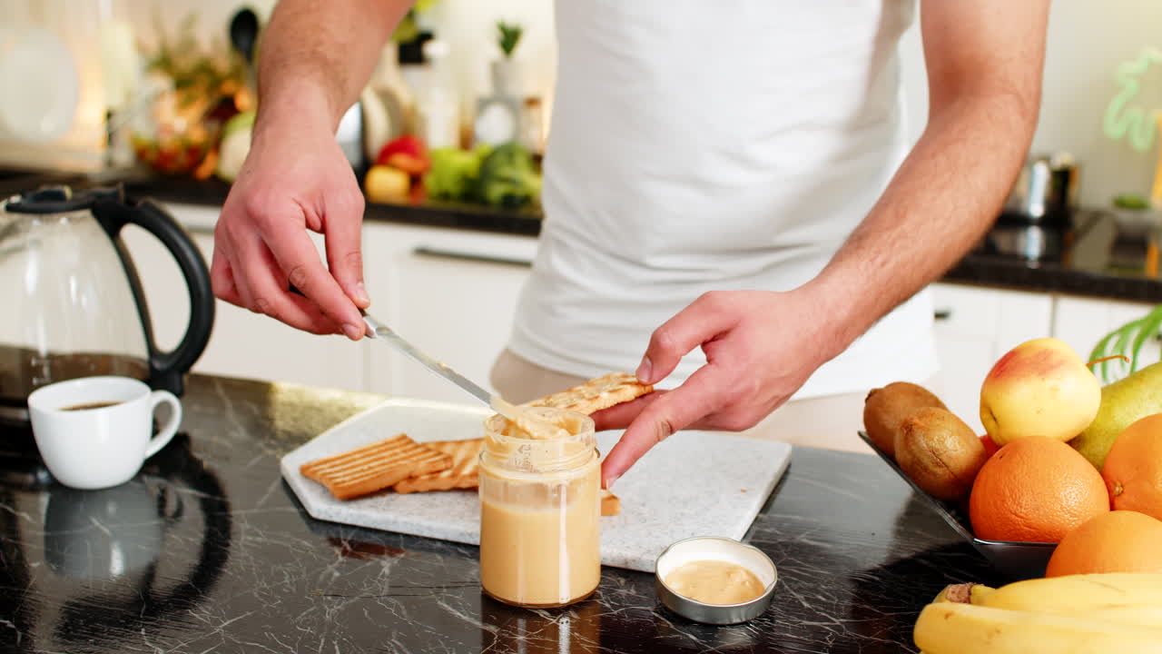 Preparing breakfast spreading peanut butter on toasted bread slice in home kitchen closeup warm shot