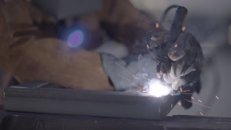 sparks fly as gloved welder fuses angle iron together, slow mo static shot