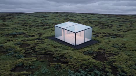 illuminated glass house stands on a vast moss covered icelandic landscape, emanating a warm glow against the twilight sky, creating a striking contrast between nature and modern architecture