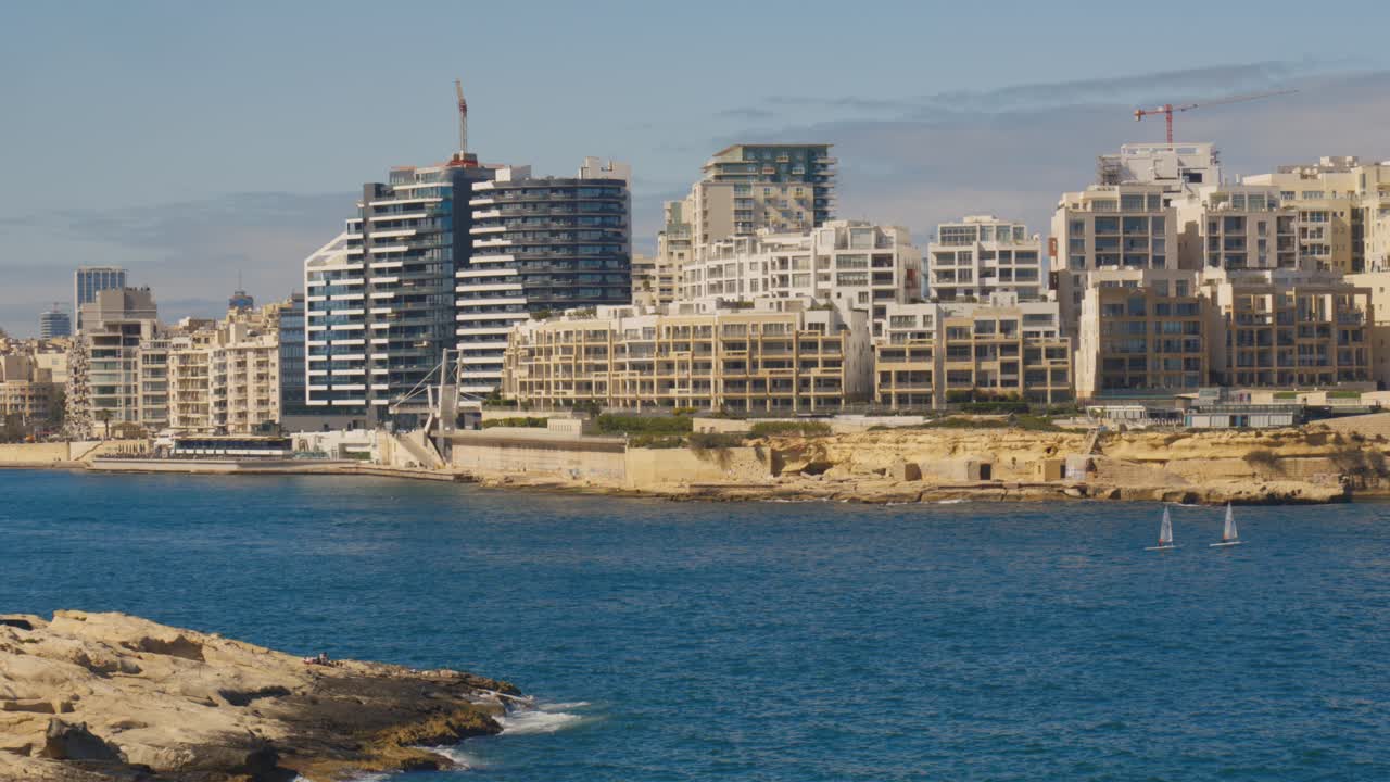Coastal view of Sliema and Tigné Point skyline with rocky shore and sailboats in Malta