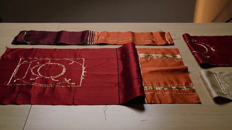 Unrolling large maroon cloth with stitched motif on wood table after roll release to reveal motif