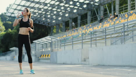 Young-Jogger-Woman-Trianing-In-The-Stadium,-Then-Stops-For-Drinking-Water-And-Keeps-On-Jogging-On-A-Summer-Morning