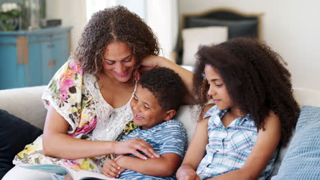 slow motion shot of mother sitting on sofa at home reading book with children