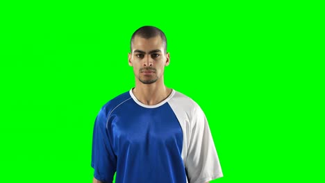 Confident-football-player-standing-against-green-screen