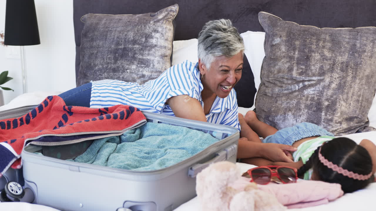 Femme métisse aux cheveux gris courts rit en faisant sa valise