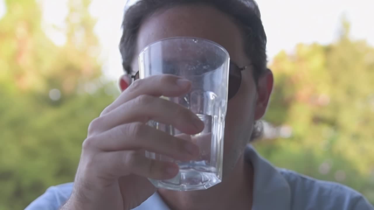 선글라스를 입은 남자가 물을 마시며 정원에서 휴식을 취하고 있으며, 배경에는 울창한 식물이 있습니다.