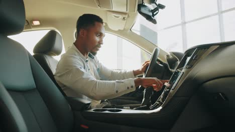 handsome young african man in denim shirt pressing touchscreen on car multimedia panel, switching shifting radio station. man using gps navigation system in car to travel. a man tests a new car