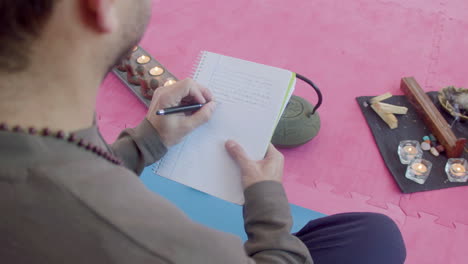 man sitting in lotus position and writing in notebook