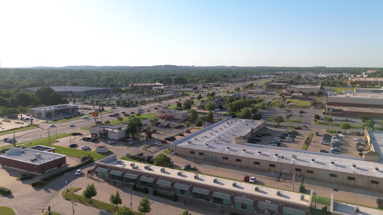 Sunny aerial view of South Tulsa, Oklahoma along South Memorial Drive, showcasing shopping centers, traffic, and suburban sprawl with a welcoming small-city vibe and everyday movement