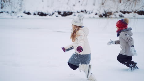 side view of two children in warm clothes and caps are running on the snowy background. active kids are playing in winter near the forest. slow motion.