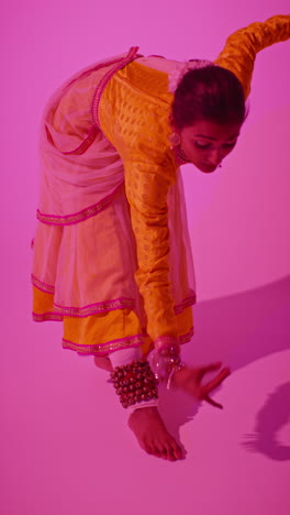 vertical video studio shot of female kathak dancer performing dance wearing traditional indian dress against purple background 1