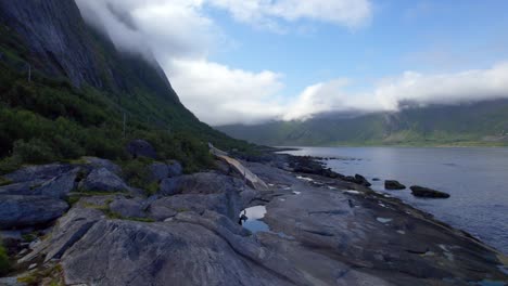 Low-aerial-dolly-forward-shot-over-the-rocky-shoreline-along-the-Tungneset-viewing-area-with-cloud-capped-mountains-along-the-coast