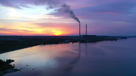 blue background of the river and industrial plant. dirty smoke from pipes against the setting sun. silhouette of a factory near the lake at sunset.