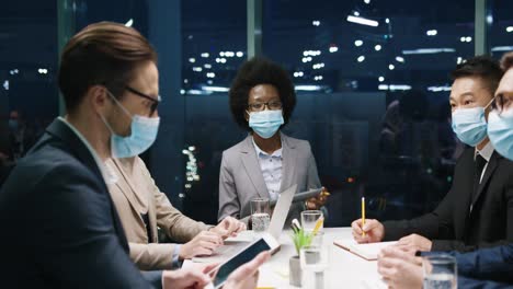 multiethnic business people group in medical masks in a team meeting in modern office and discussing about a project