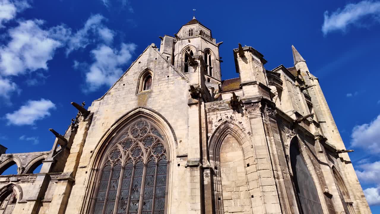 Wide view of the gothic Church of Saint-Étienne-le-Vieux with large stained-glass windows and detailed facade under blue sky, Caen, Normandy, France.