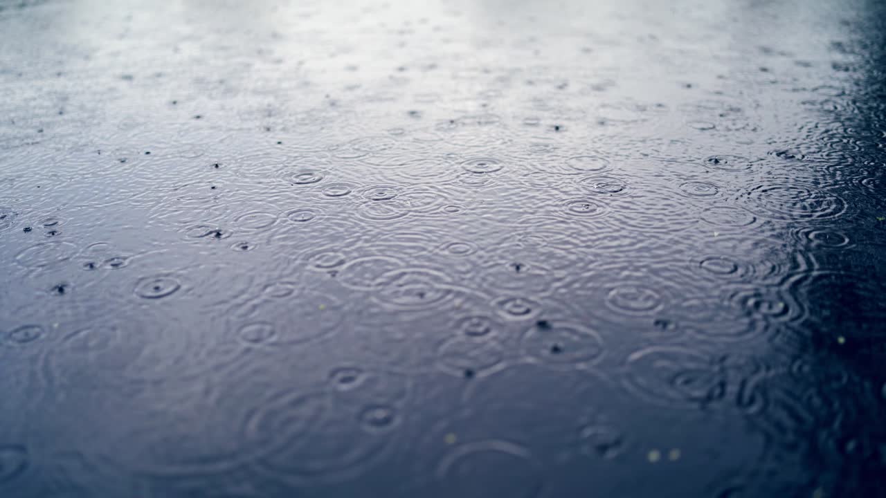 Many drops of rain are falling into the blue water outdoors.