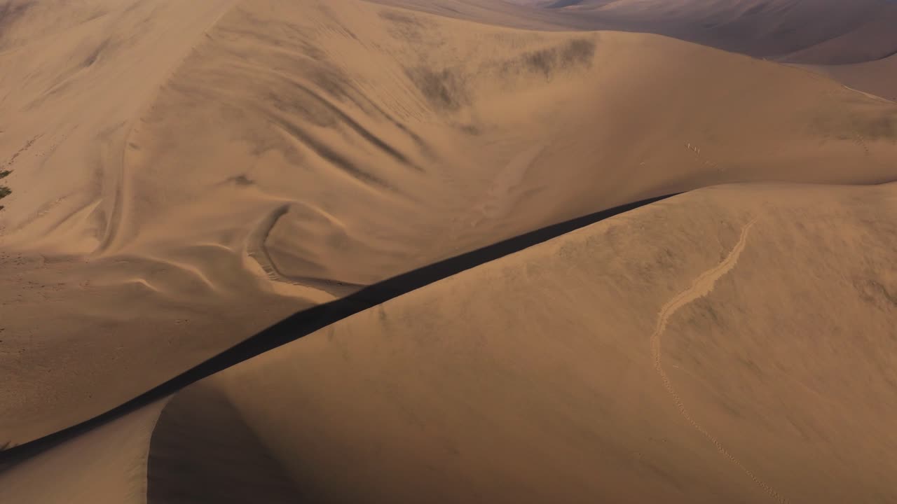 Sunlit dune ridge cuts diagonally with crisp shadows defining its curving form, orbit establishes shade