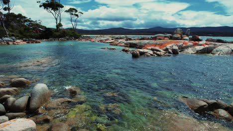 bay of fires drone flys towards orange boulders tasmania, australia