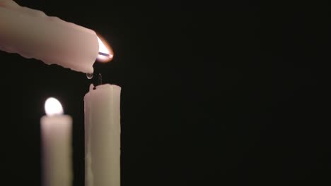 una vela blanca encendiendo una vela blanca con una vela encendida en el fondo