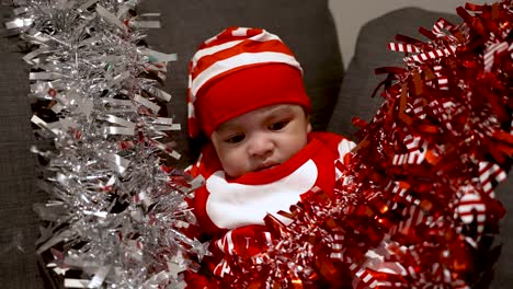 adorable 2 month old baby boy wearing red christmas outfit and hat surrounded by red and silver tinsel