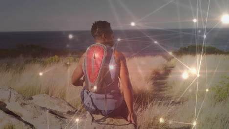 man sitting on rock wearing hydration pack facing ocean trail, showing technology network overlay