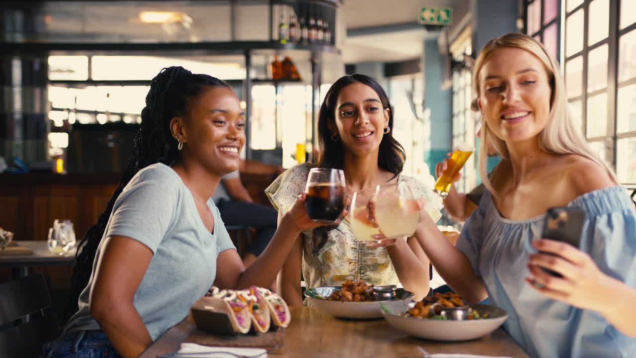 Group Of Female Friends Meeting Up In Restaurant Posing For Selfie On Mobile Phone With Food