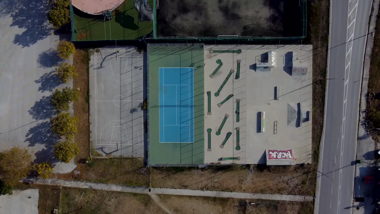 Aerial top down descent over outdoor sports facilities with tennis, basketball, mini golf and skate park