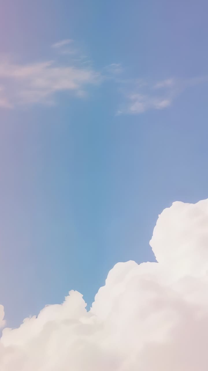 Vertical video: Panning camera showing billowy cumulus clouds in open sky, shifting blue to pink