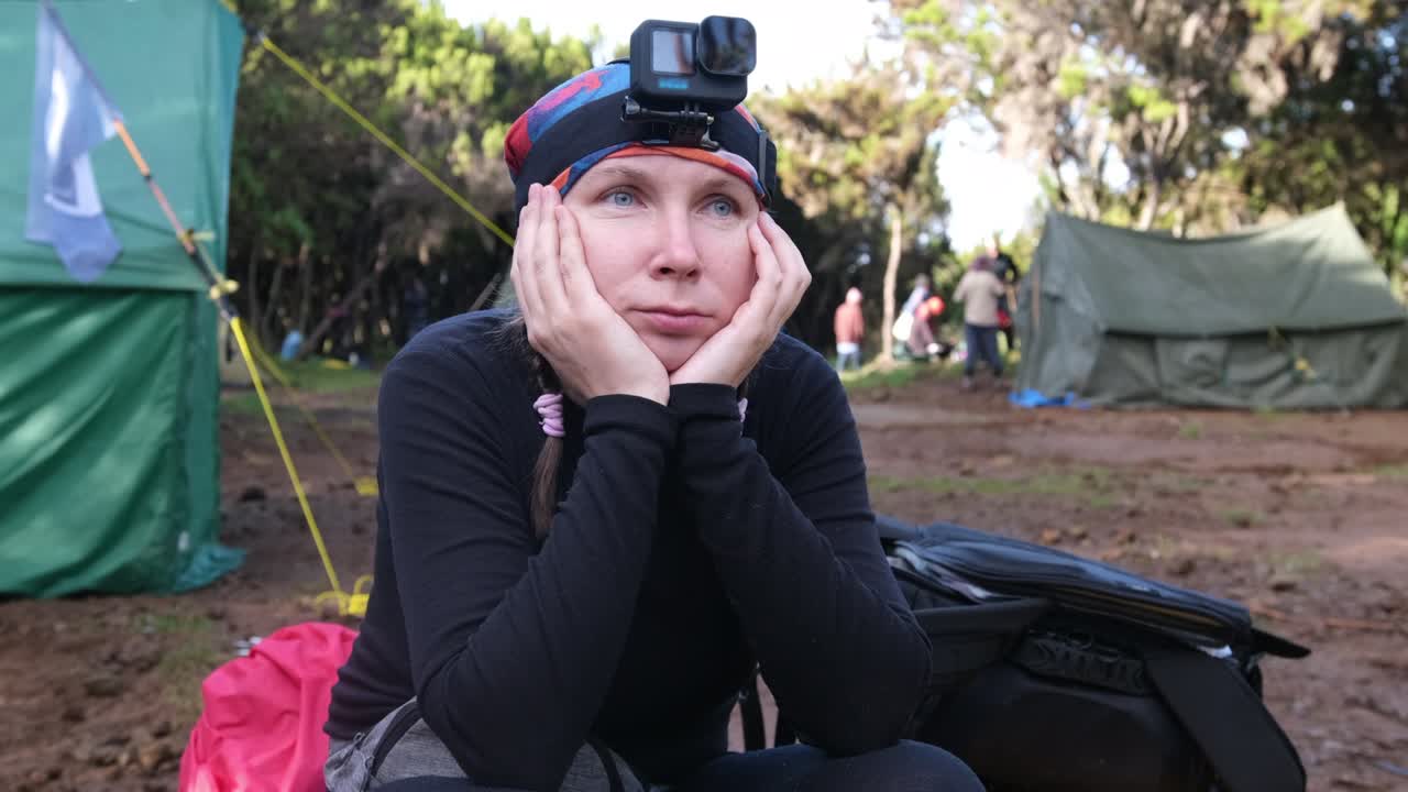 A hiker with action cams on her head sits on bags and waits for the group