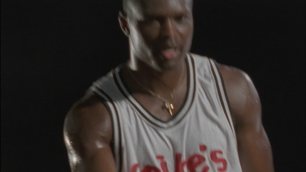 un hombre lanza una pelota de baloncesto, sonríe y la recoge, la lanza de nuevo y hace una mueca