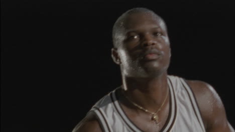 un hombre lanza una pelota de baloncesto, sonríe y la recoge, la lanza de nuevo y hace una mueca