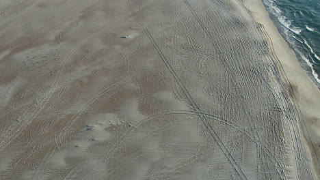 Drone-shot-of-an-empty-beach-in-the-winter,-starting-on-the-sand-then-titling-up-to-reveal-beach-and-ocean