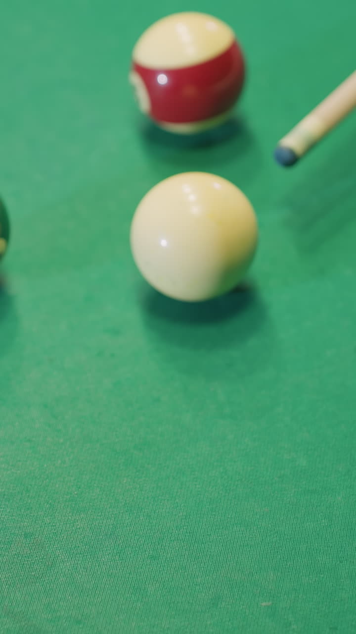 el palo del taco golpea la pelota de billar blanca en la mesa de billar verde mientras las bolas de colores están esparcidas. la mano agarra el taco, lista para un disparo preciso. el disparo de primer plano captura el movimiento y los detalles del juego de billar