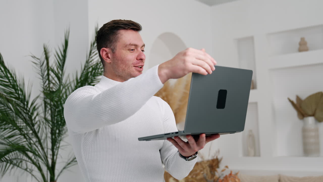 Caucasian man finishes video chat on his laptop and closes gadget. Man is happy to end up work.