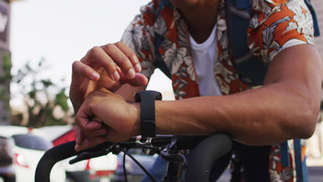 african american man in city, sitting on bike in street using smartwatch